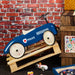 Retro blue police ride-on car for toddlers with white wheels against brick wall backdrop