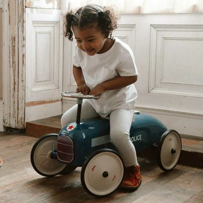 Toddler riding a blue retro police ride-on car toy indoors on wooden floor