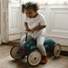 Toddler riding a blue retro police ride-on car toy indoors on wooden floor