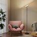 Pink armchair with a patterned pillow next to a standing lamp in a room with beige walls and wooden floor.