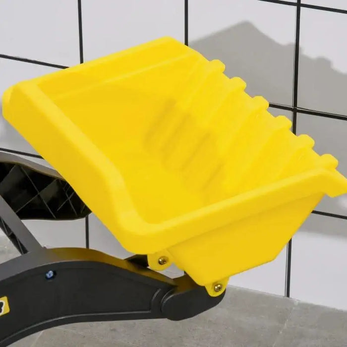 Yellow plastic excavator bucket on black metal arm, tiled wall background