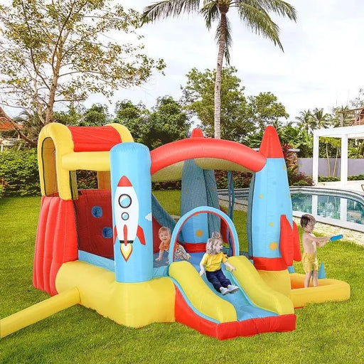 Kids playing on rocket bouncy house with dual slides and pool in a backyard garden
