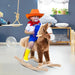 Smiling child in cowboy outfit riding a brown rocking horse toy in a playroom