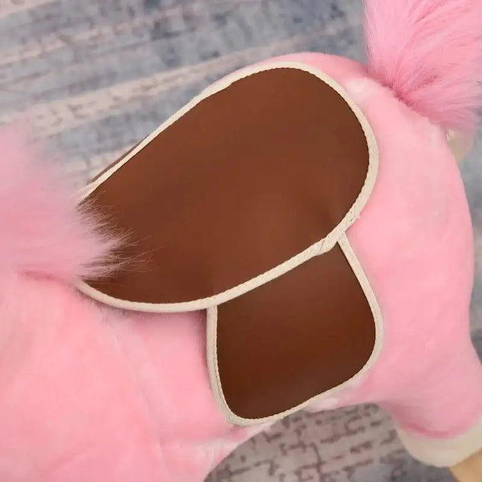 Close-up of pink rocking horse with brown saddle and fluffy pink tail on carpet