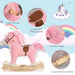 Pink and white plush rocking horse with saddle, wooden handles, and foot pedal on pastel background.