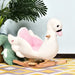 Plush white and pink swan rocking horse for kids on patterned rug with palm leaf plant