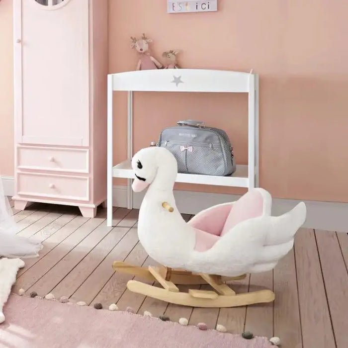 Plush pink and white swan rocking horse in a pastel nursery with wooden floor.