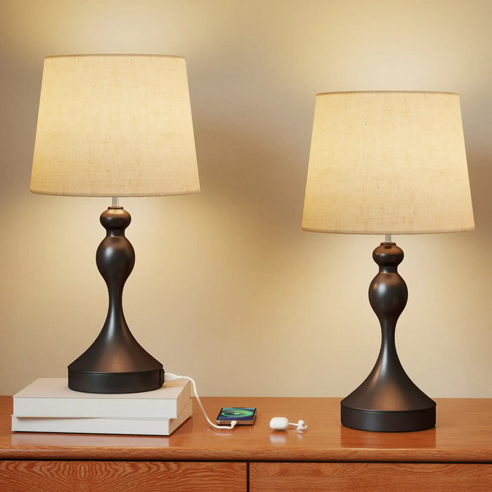 Two table lamps with beige shades on a wooden surface against a beige wall.