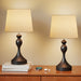 Two table lamps with beige shades on a wooden surface against a beige wall.