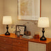 Two table lamps on a wooden dresser with decorative items and a framed picture in the background.