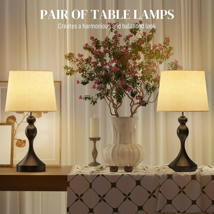 Pair of table lamps on a decorative table with a vase and flowers in the center.