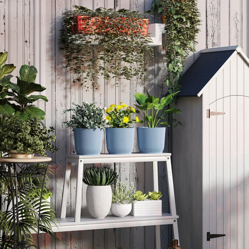White wooden plant stand with three blue ribbed stackable pots with indoor plants on top, surrounded by greenery