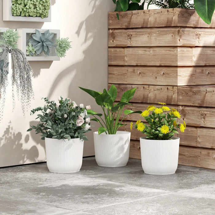 Set of 3 white stackable plastic plant pots with green and yellow indoor plants by wooden wall