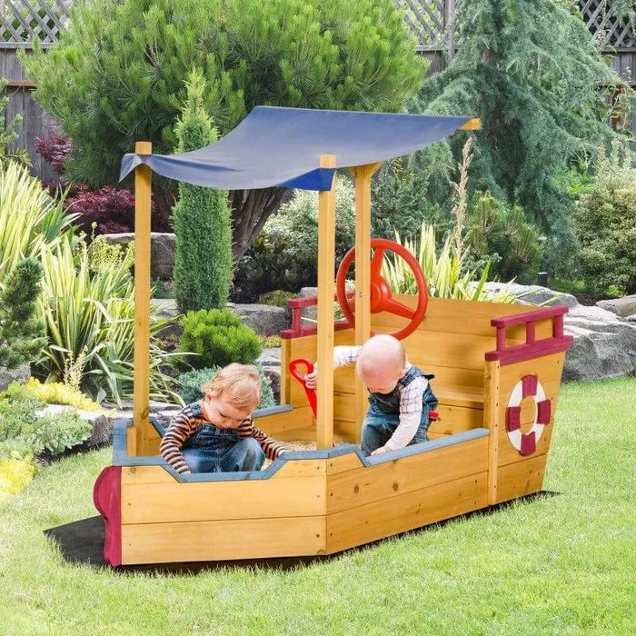 Kids playing in wooden ship sandbox with canopy and storage bench in garden