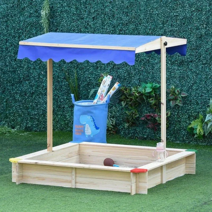 Square wooden sandbox with adjustable blue canopy in garden, toys and storage bin nearby.