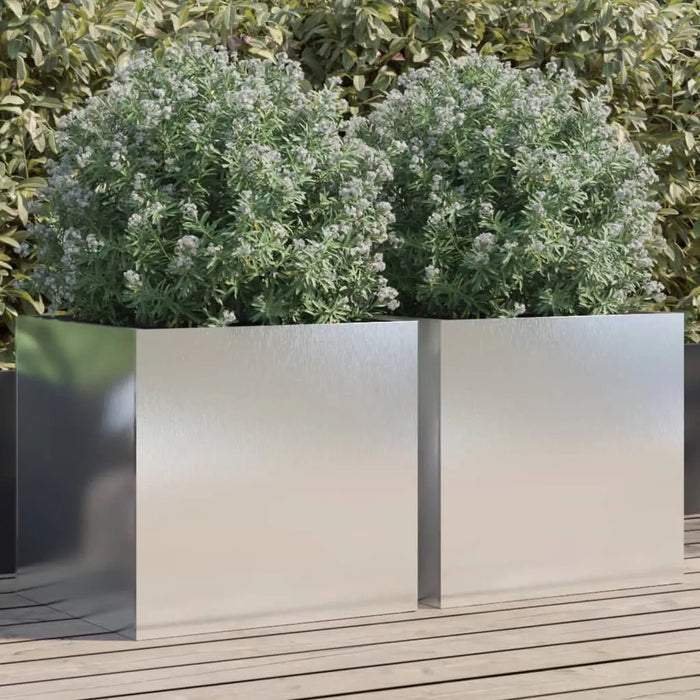 Two silver stainless steel garden planters with green leafy plants on wooden deck outdoors