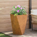 Large weathering steel outdoor garden planter with vibrant pink flowers on patio next to cushioned wicker chair