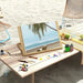 Beechwood tabletop easel with painting supplies on beach, palm tree artwork displayed