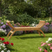 Teak outdoor wooden garden bench with curved armrest design surrounded by lush colorful flowers and green grass