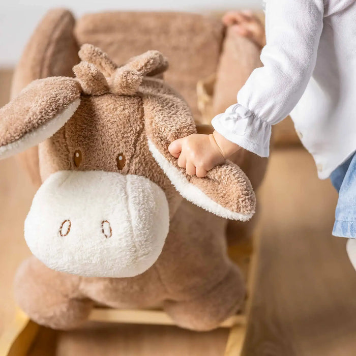 Child holding ear of beige teddy rocker donkey plush toy with safety harness at Little and Giant Explorers