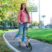Teen riding green kick scooter with folding design and dual brake on park path