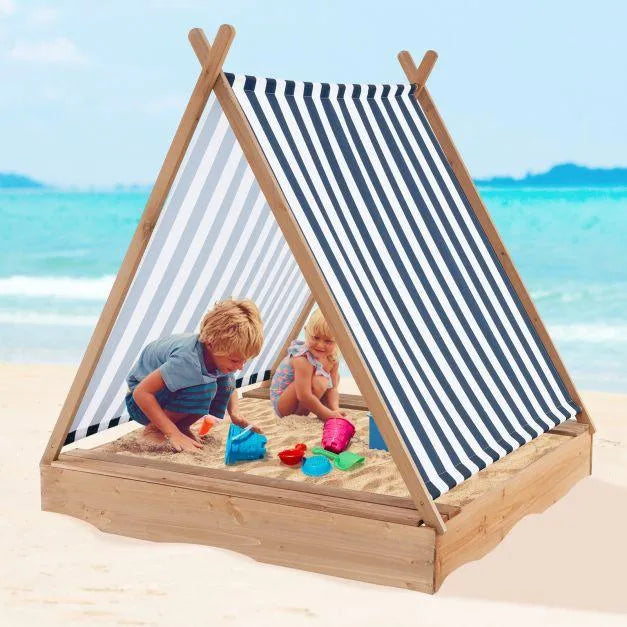 Kids playing in wooden teepee sandbox with striped sun cover on a sandy beach