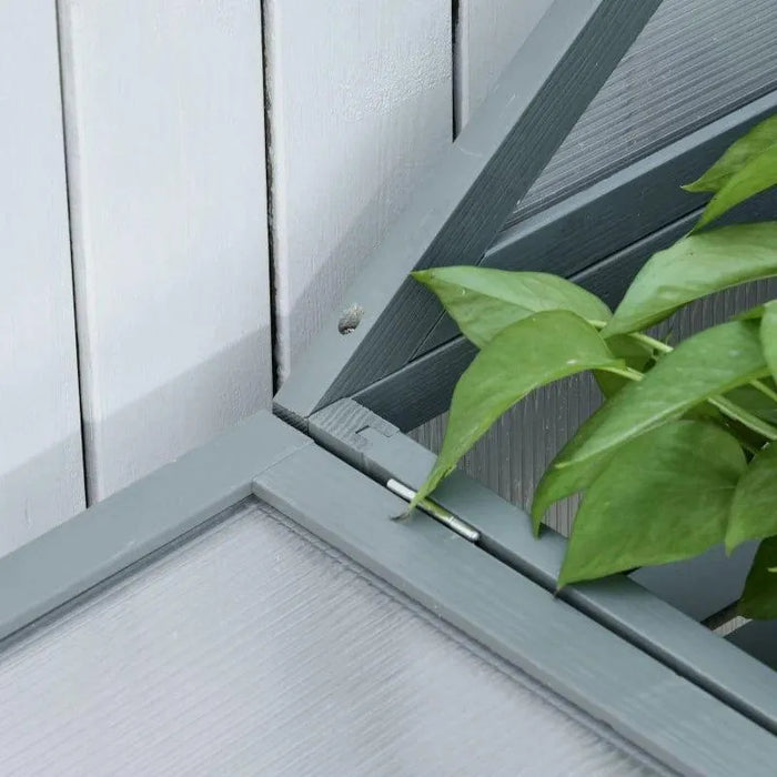 Detail of grey wooden mini greenhouse corner with green plant leaves inside