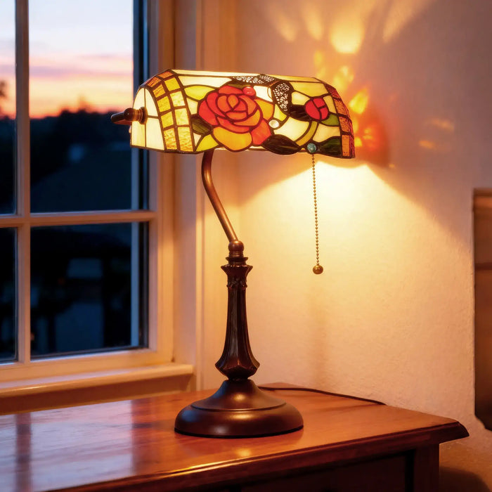 Decorative table lamp with stained glass shade on a wooden surface near a window.