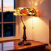 Decorative table lamp with stained glass shade on a wooden surface near a window.
