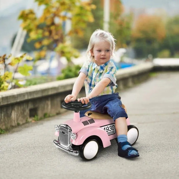Toddler riding pink foot-to-floor ride-on car outdoors, vintage style toy vehicle.