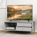 Light grey TV cabinet with open drawers and drop-down door, gold legs and knobs, holding camera and books