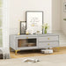 Light grey TV cabinet with gold legs and knobs, featuring drawers, drop-down door with tempered glass, decorated with lamp, vases, framed art, and flowers