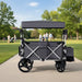 Black and gray outdoor wagon with canopy on a paved path in a park.