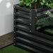 Two-tier dark grey galvanized steel raised garden bed with green plants on artificial grass and wooden flooring