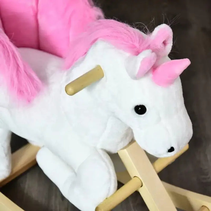 White and pink plush unicorn rocker toy with wooden handles on dark floor
