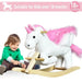 Toddler playing beside white and pink plush unicorn rocker toy for kids over 18 months