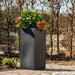 Tall black double-walled flower pot with green plants, outdoor garden setting