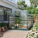 Walk-in greenhouse with green aluminum frame, sliding door, and roof vent on patio