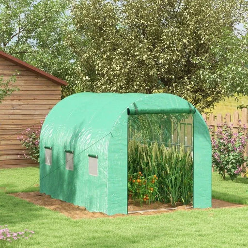 Green polytunnel greenhouse with plants inside in a sunny garden with trees and a wooden shed