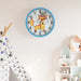 Children's wall clock with a fox design on a wall in a room with toys and a shelf.