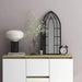 Modern wooden sideboard with white doors featuring decorative lamp, glass vase with greenery, black arched window mirror, and classic alarm clock