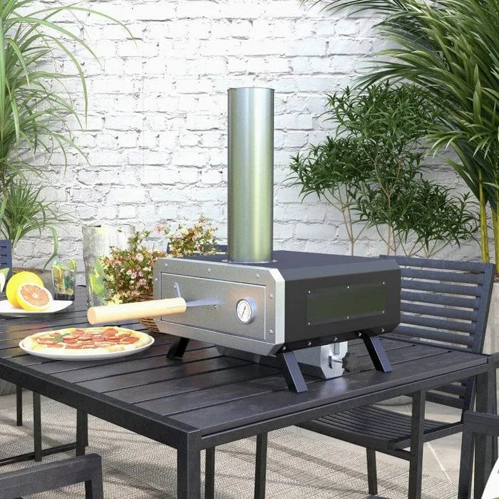 Wood-fired rotating pizza oven with chimney on a patio table, surrounded by plants