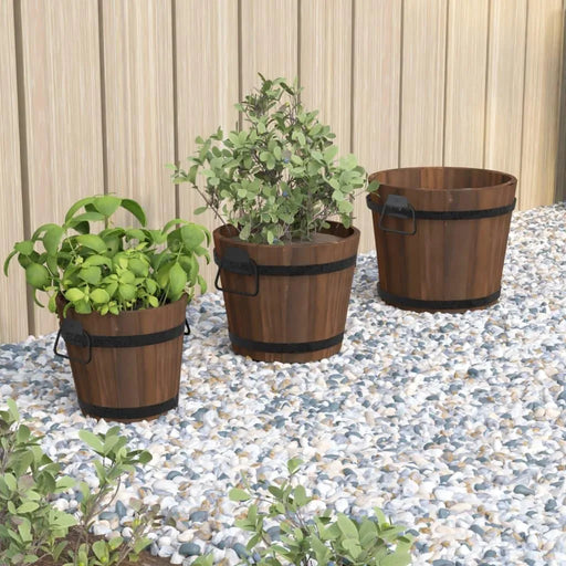 Wooden bucket planter set in three sizes with metal handles on gravel by a wooden wall