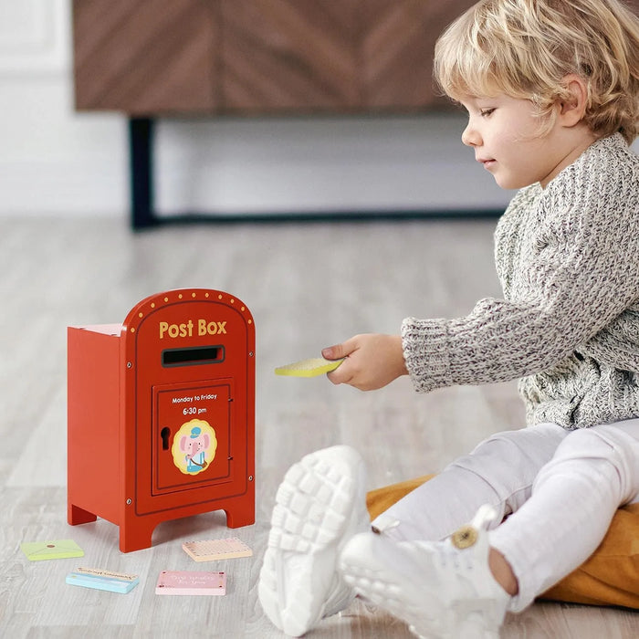 Child playing with a red toy post box on a light-colored floor.