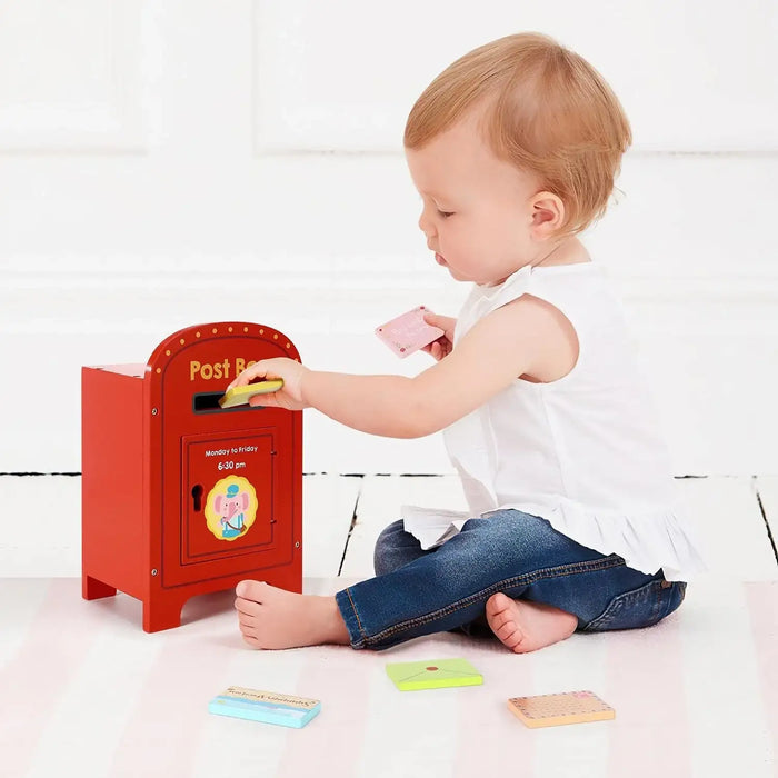 Child playing with a red toy post box on a white floor.