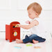 Child playing with a red toy post box on a white floor.