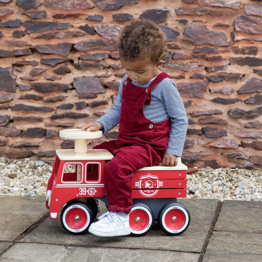 Toddler riding red wooden fire truck toy with anti-tilt safety system outdoors