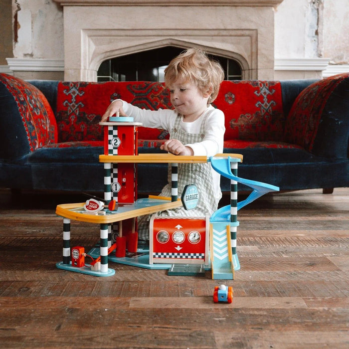 Child playing with Vilac wooden three-level toy garage and vehicle playset on wooden floor