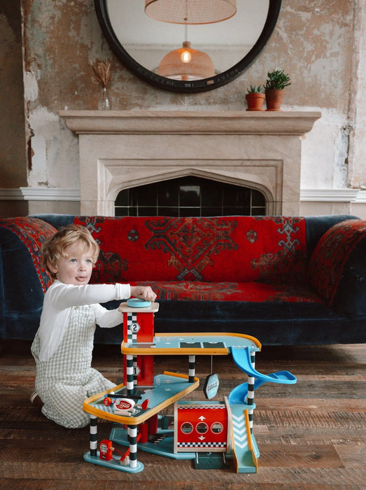 Child playing with wooden three-level toy garage and car playset in cozy living room