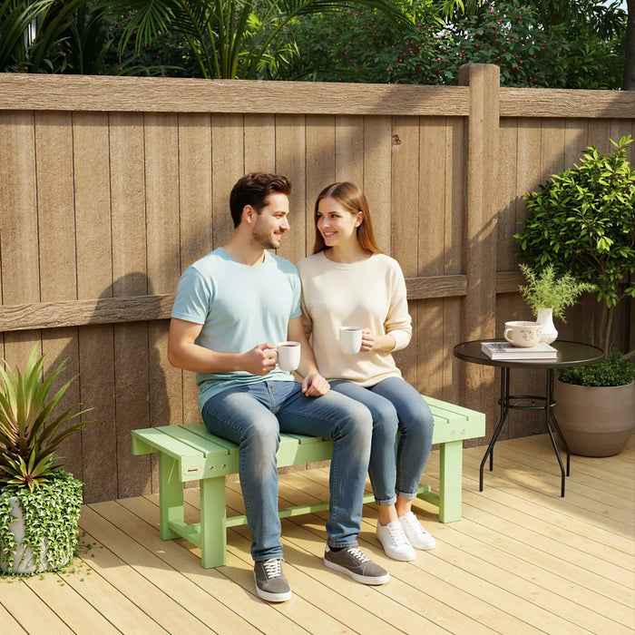 Couple enjoying coffee seated on light green wooden garden bench on patio with round black side table and plants